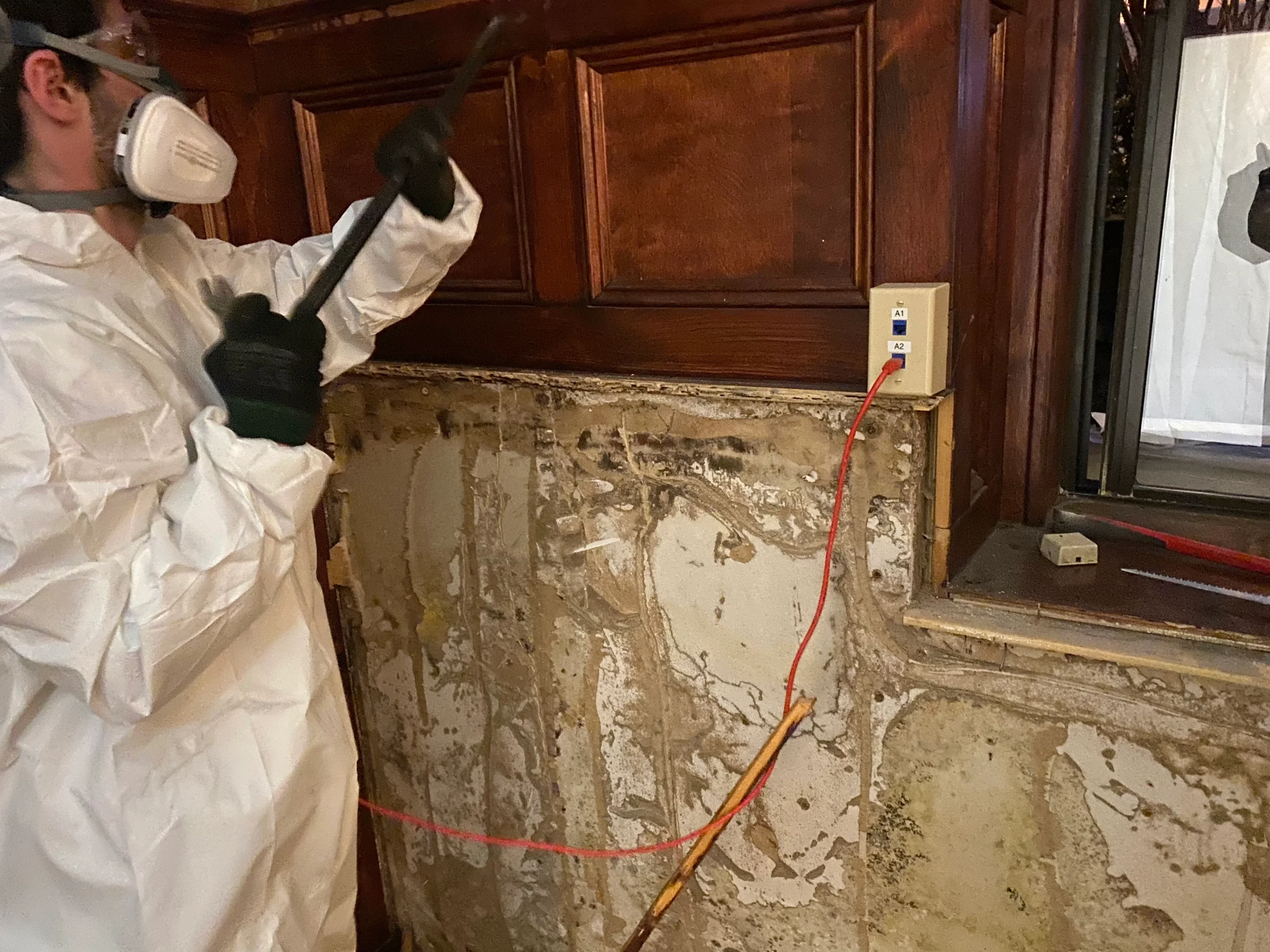 Mold Men NJ Employee in full PPE remediating mold from behind a wall Mold Men NJ Employee in Morris Township, NJ in full PPE remediating mold from behind a wall